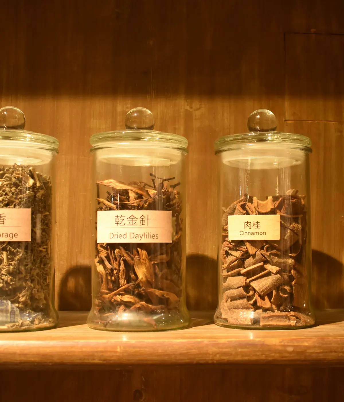 Glass jars filled with dried herbs on a wooden shelf